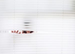 person avoiding other people by peaking through blinds