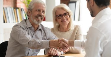 Happy old couple clients make financial deal handshake meeting lawyer