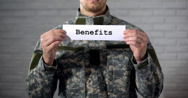 Benefits word written on sign in hands of male soldier, veterans support, aid